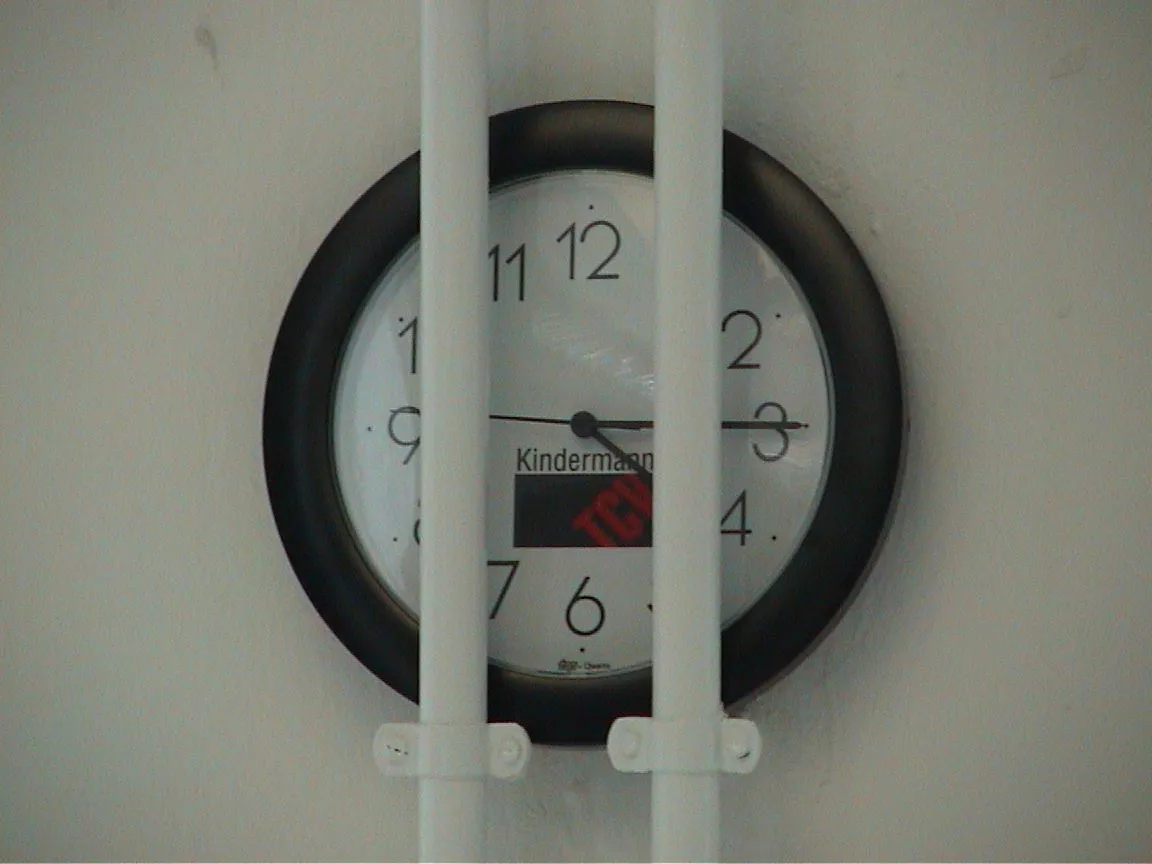 A clock stuck behind two heating pipes points at a quarter past four.