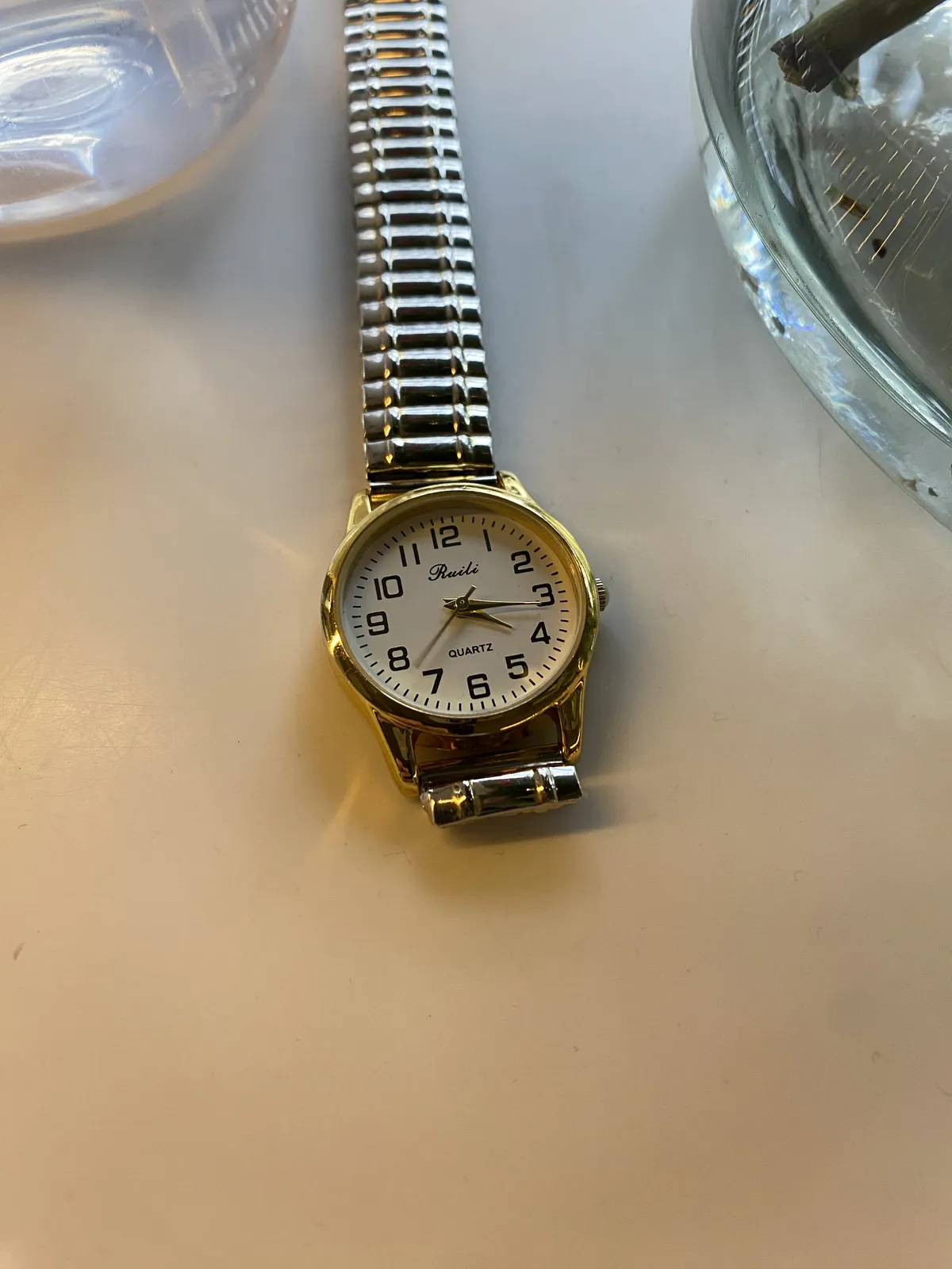 A little gold coloured wrist watch — Ruili Quartz it says on its face — on a table. It points at 16 minutes past 4.
