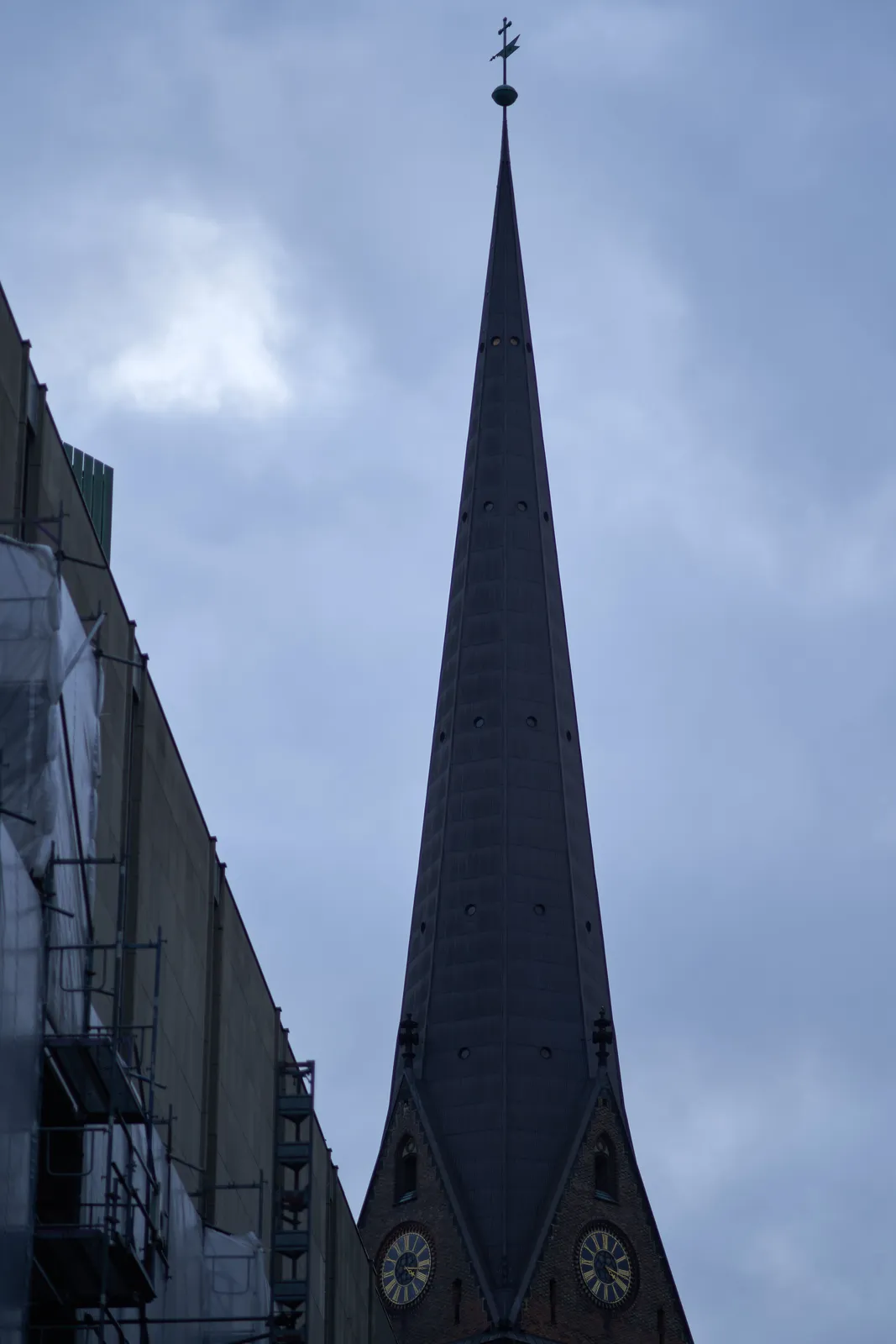 A high, thin, very pointy church tower with a clock. The clock points at 17 minutes past 4.