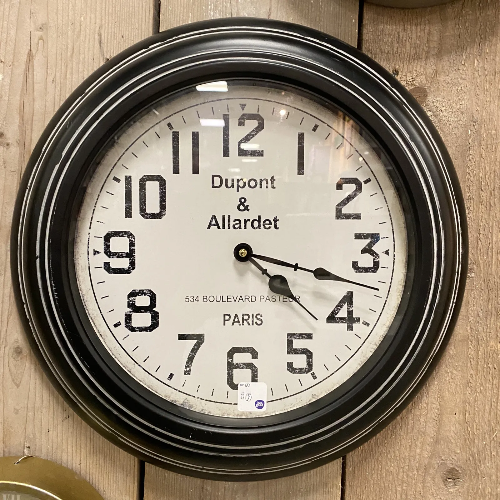 A clock with the words Dupont & Allardet, 534 Boulevard Pasteur, Paris printed on its face. The hands are classical. They point at 17 minutes past 4.