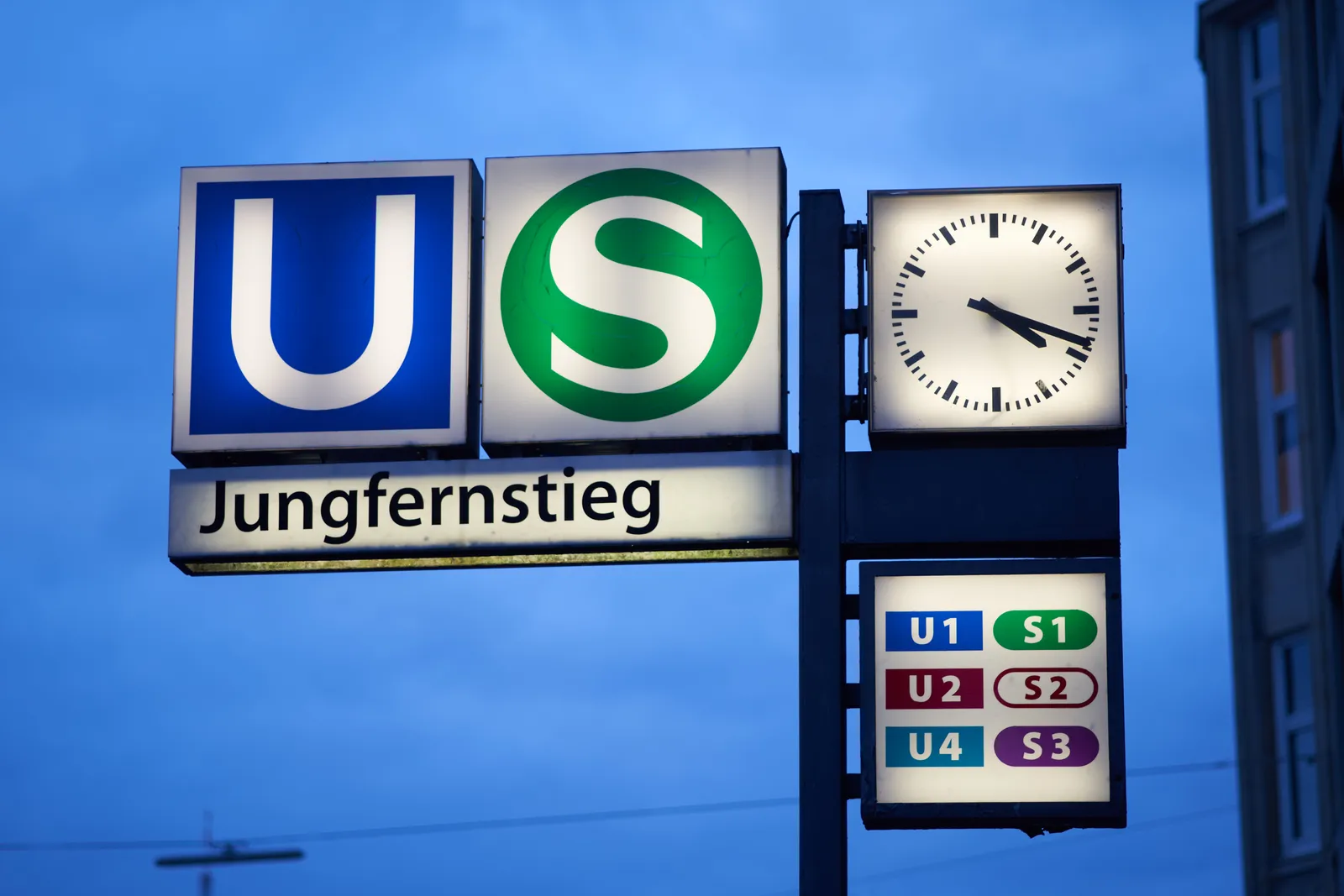 A lit sign that indicates that here, at Jungfernstieg station you can find the U-bahn trains number U1, U2 and U4, and S trains S1, S2 and S3. The clock points at 18 minutes past 4, so no need to hurry.