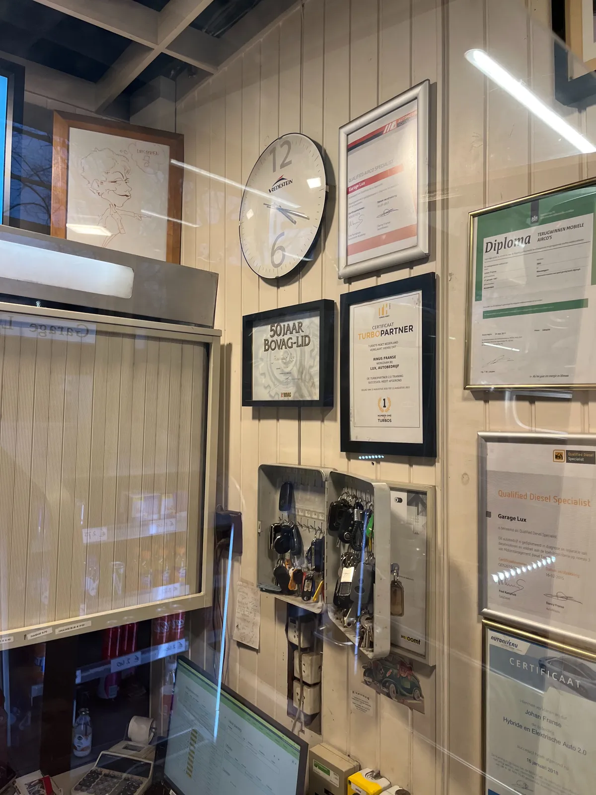 All kinds of certificates are pinned to a wall. Among these certificates hangs a clock. It points at 19 minutes past 4.