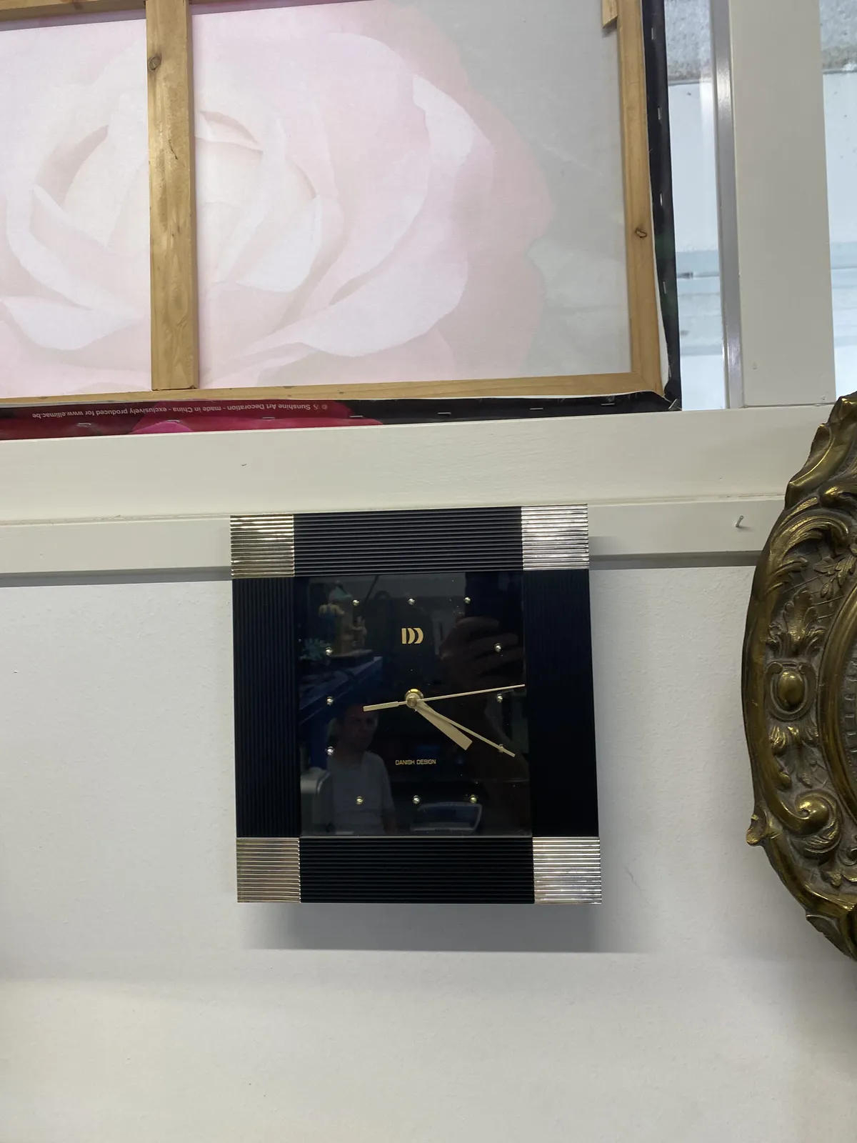 A black clock with the words Danish Design printed on its face. It points at 20 past 4. 