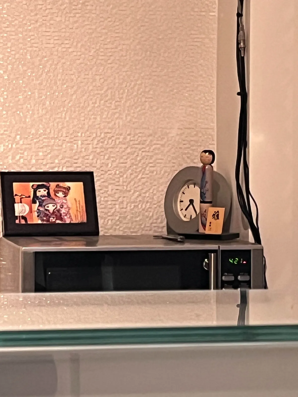 A small Japanese statue and a frame with a picture of some Japanese cartoon characters in it, stand on a microwave oven, together with a little clock. This clock points at 24 minutes past 7. The microwave’s own clock says it’s 21 minutes past 4. One of them is correct.