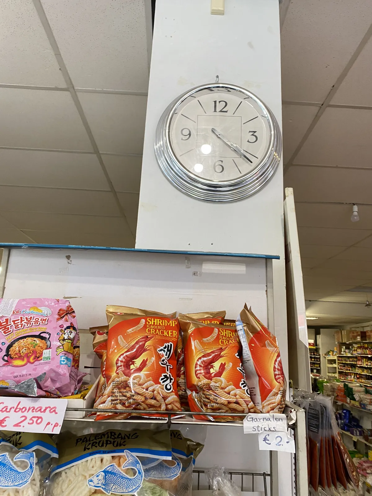 Bags with eastern snacks in a rack. Above this rack there’s a clock which points at 22 minutes past 4. 