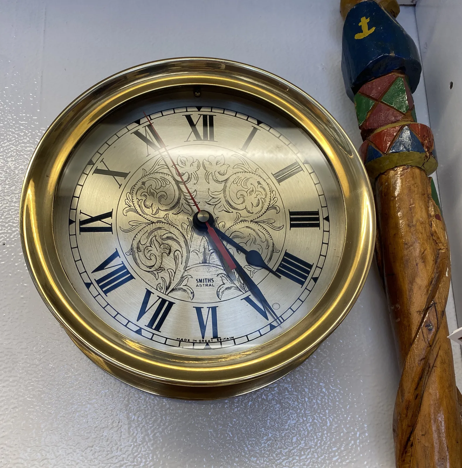 The face of this clock is finely etched, with leave-like ornaments, and roman numerals. It’s framed in a brass circle, and it points at 24 minutes past 4.