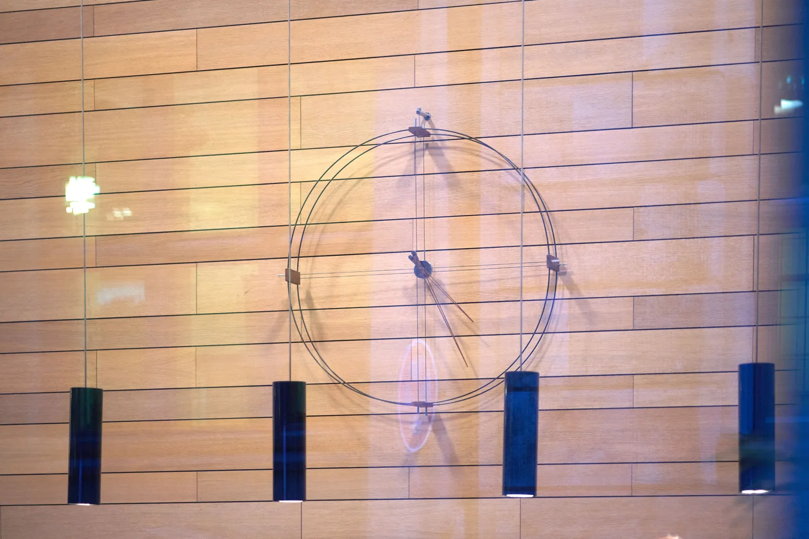 A minimalist clock on a wooden wall. The clock points at approximately 25 minutes past 4.