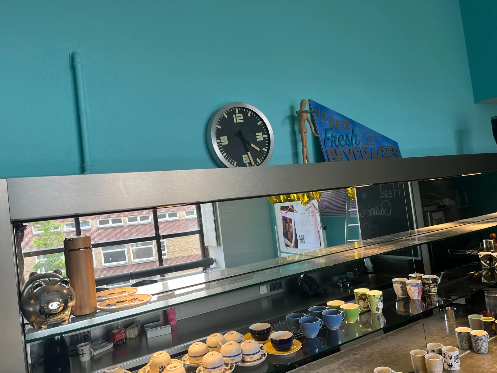 A blue wall, a counter with coffee cups, and a clock. On the clock it’s 27 minutes past 4.