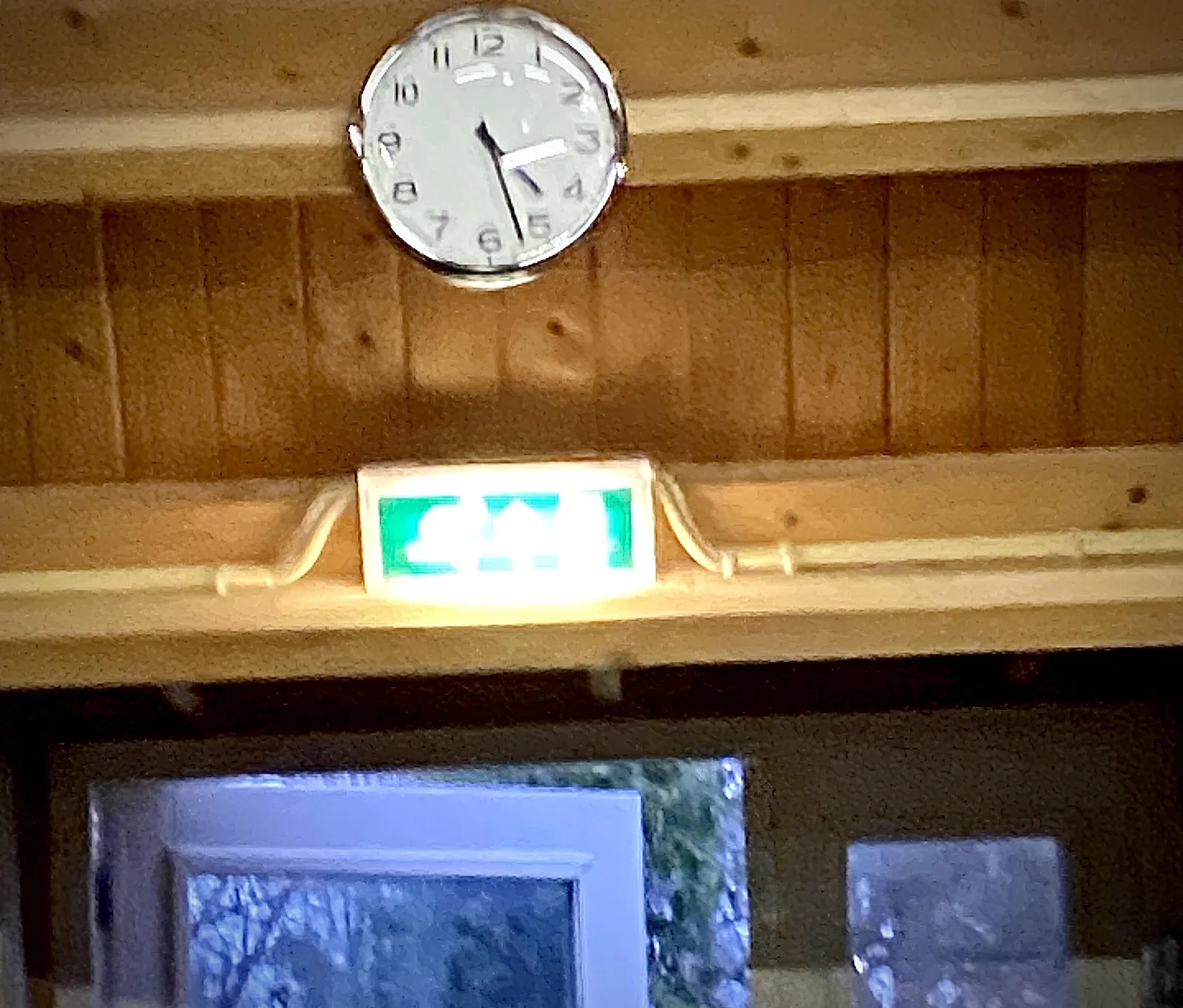 A blurry picture, taken in a wooden shed. There’s a clock, above the exit sign, that seems to point at approximately 27 past 4.