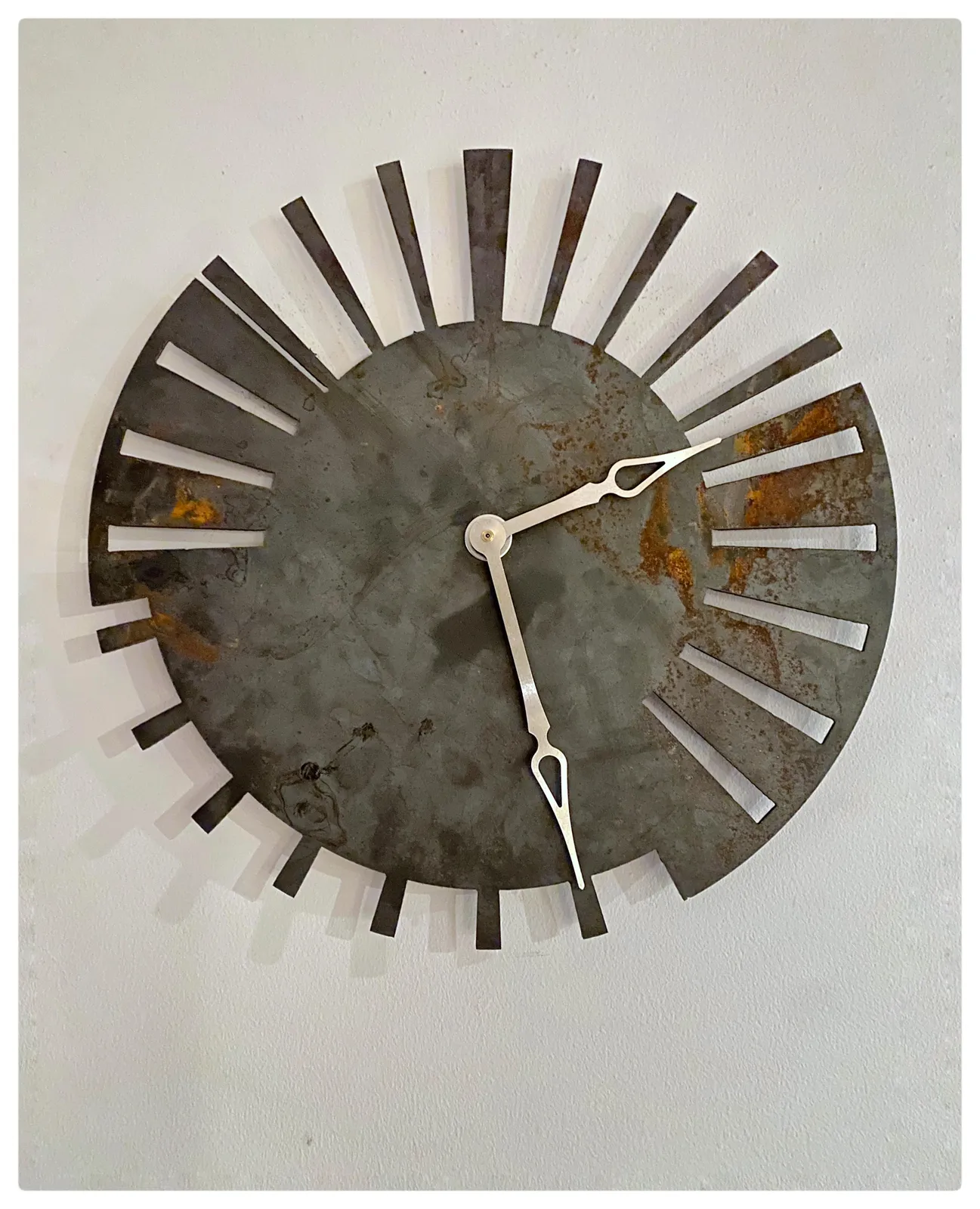 A minimalist, yet complex, and very smart clock. It is able to show at what time the sun rises and at what time it sets, on both the longest, and on the shortest days of the year. It’s cut out of one sheet of metal, a bit rusty in places. It’s a 24 hour clock, so once you know that, you can see that it points at 27 minutes past 4.