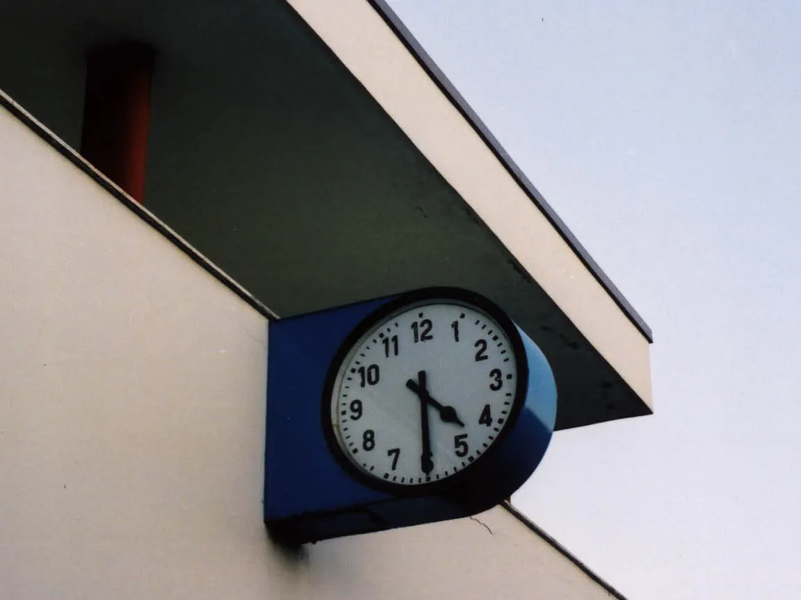 A clock attached to a building points at half past four.