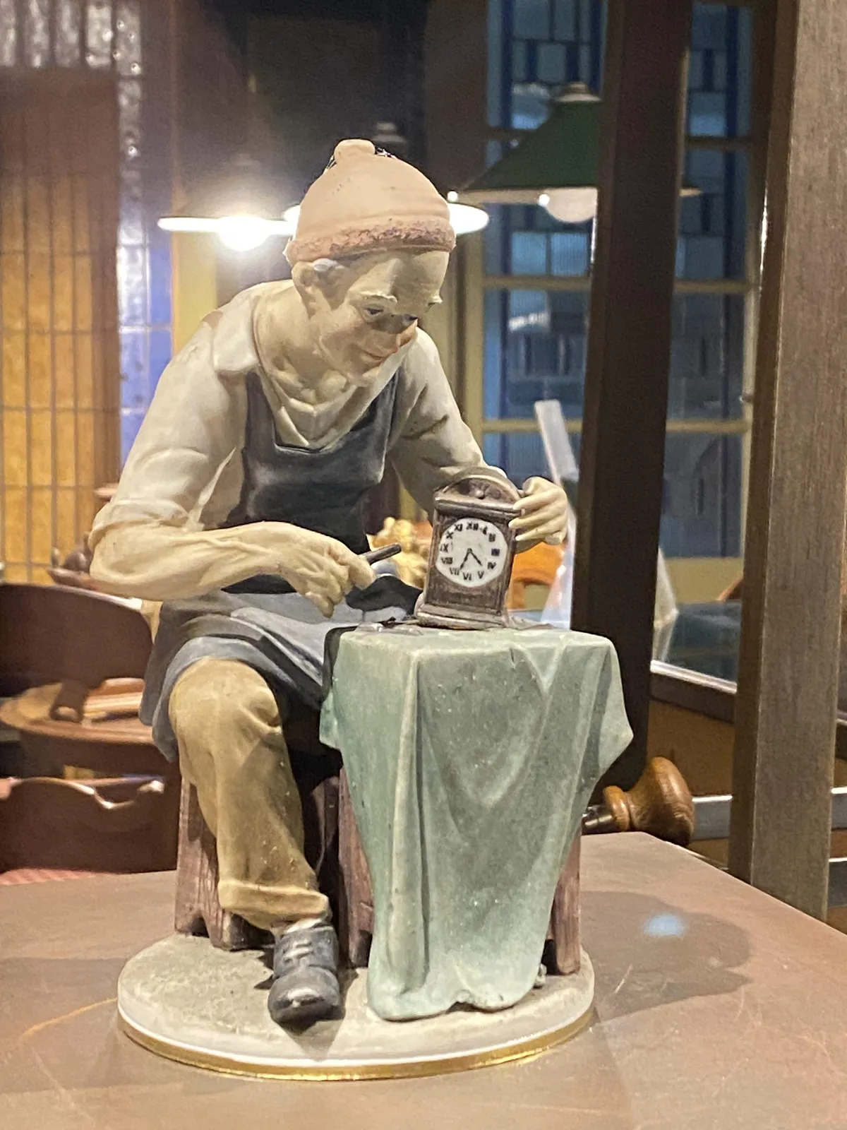 A little, painted statue of a clock maker who is working on a clock. This clock points at 33 minutes past 4.