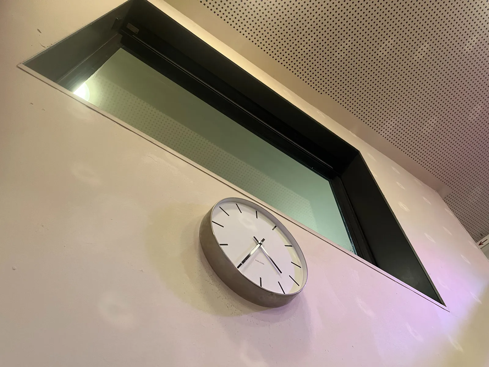 A picture taken from below, there’s quite some perspective distortion. Below a window there’s a clock that points at 25 minutes to 5.