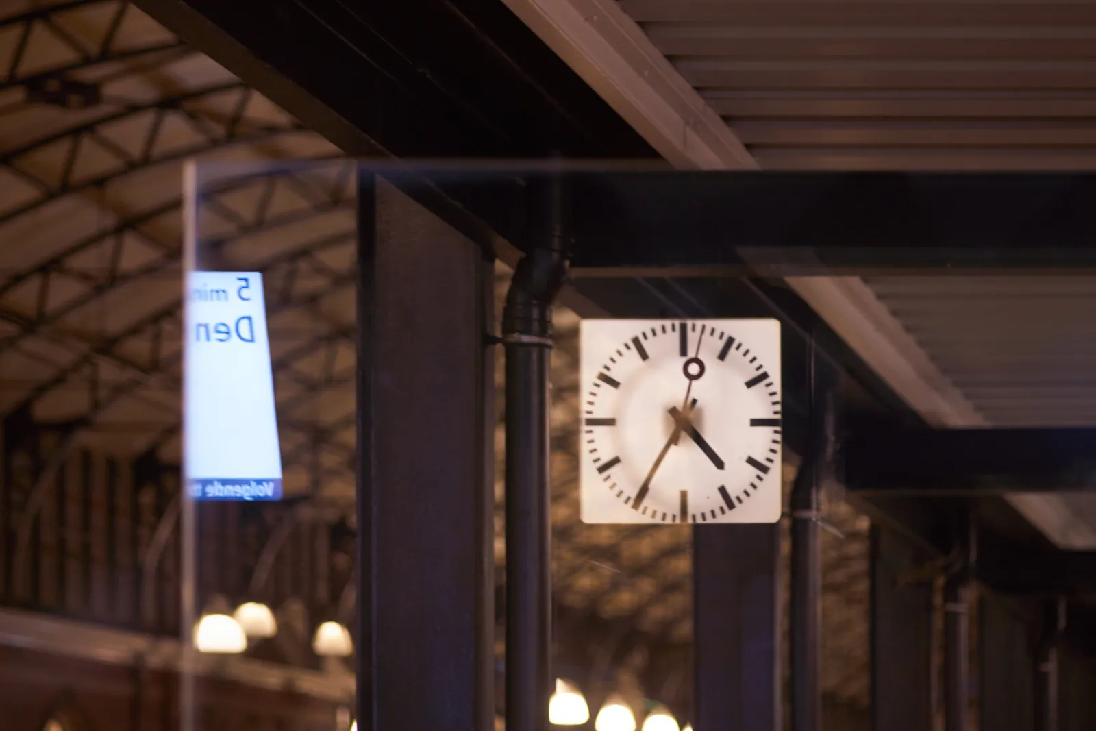 In the reflection of a glass pane on a station, a clock can be seen. It looks like it points at 35 past four.
