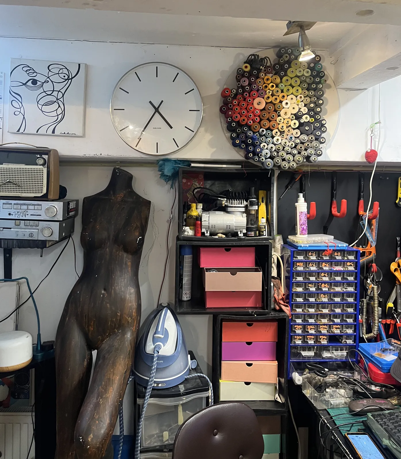 A peek into the workshop of someone with seems to work with fabrics. Among the yarn, the tailors’s dummy and all kinds of tools, there’s a clock that points at 35 minutes past four.