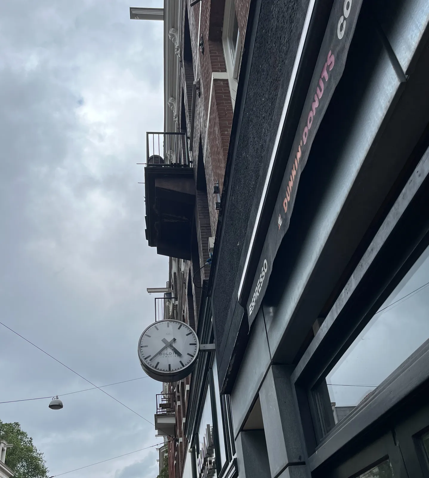 A clock attached to a facade of a shop. It points at 22 minutes to 5.