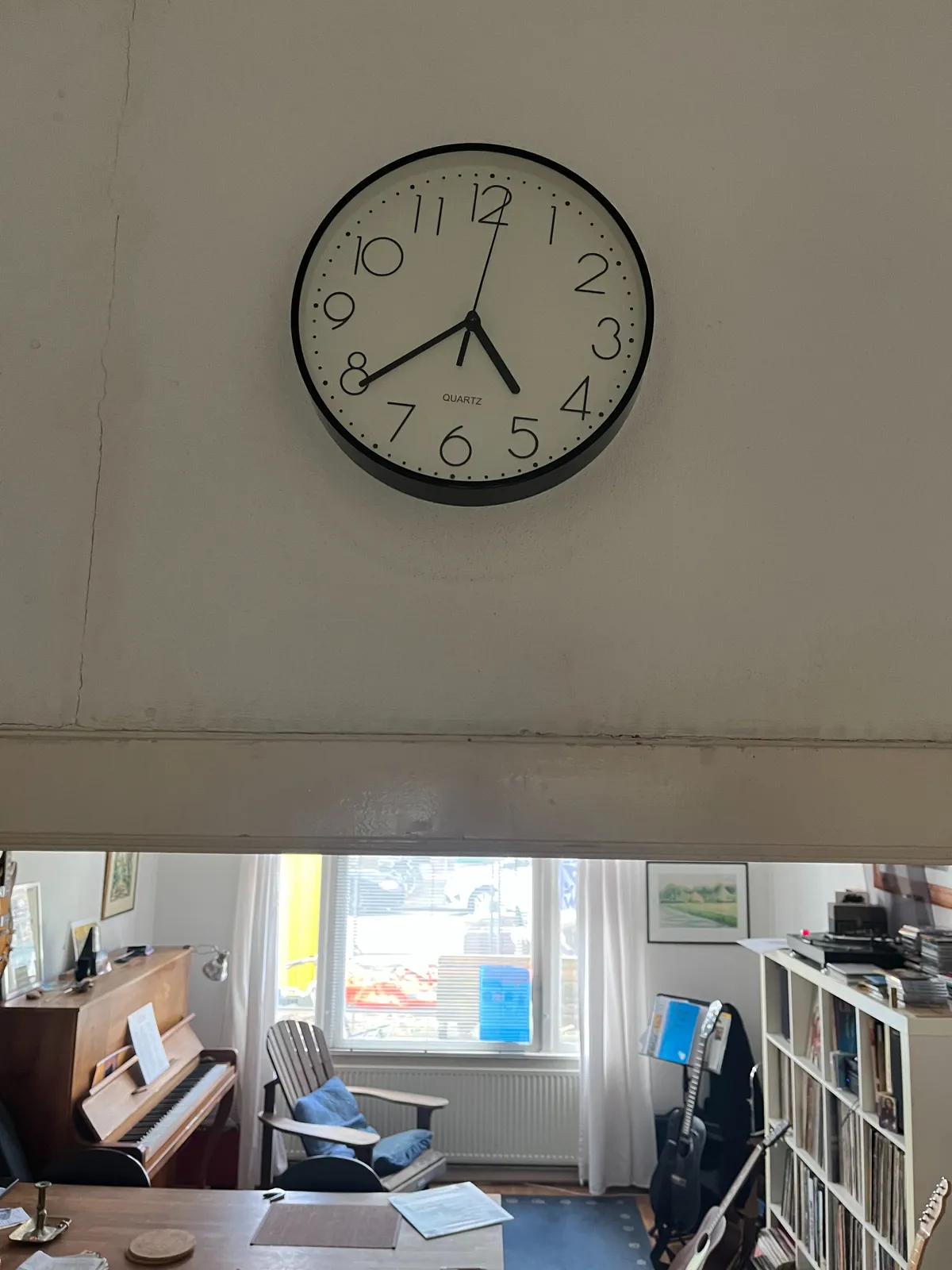 Above a door to a music room, with a stereo, lots of vinyl records, guitars and a piona, above this door there’s a simple wall clock that points at 21 minutes to 5.