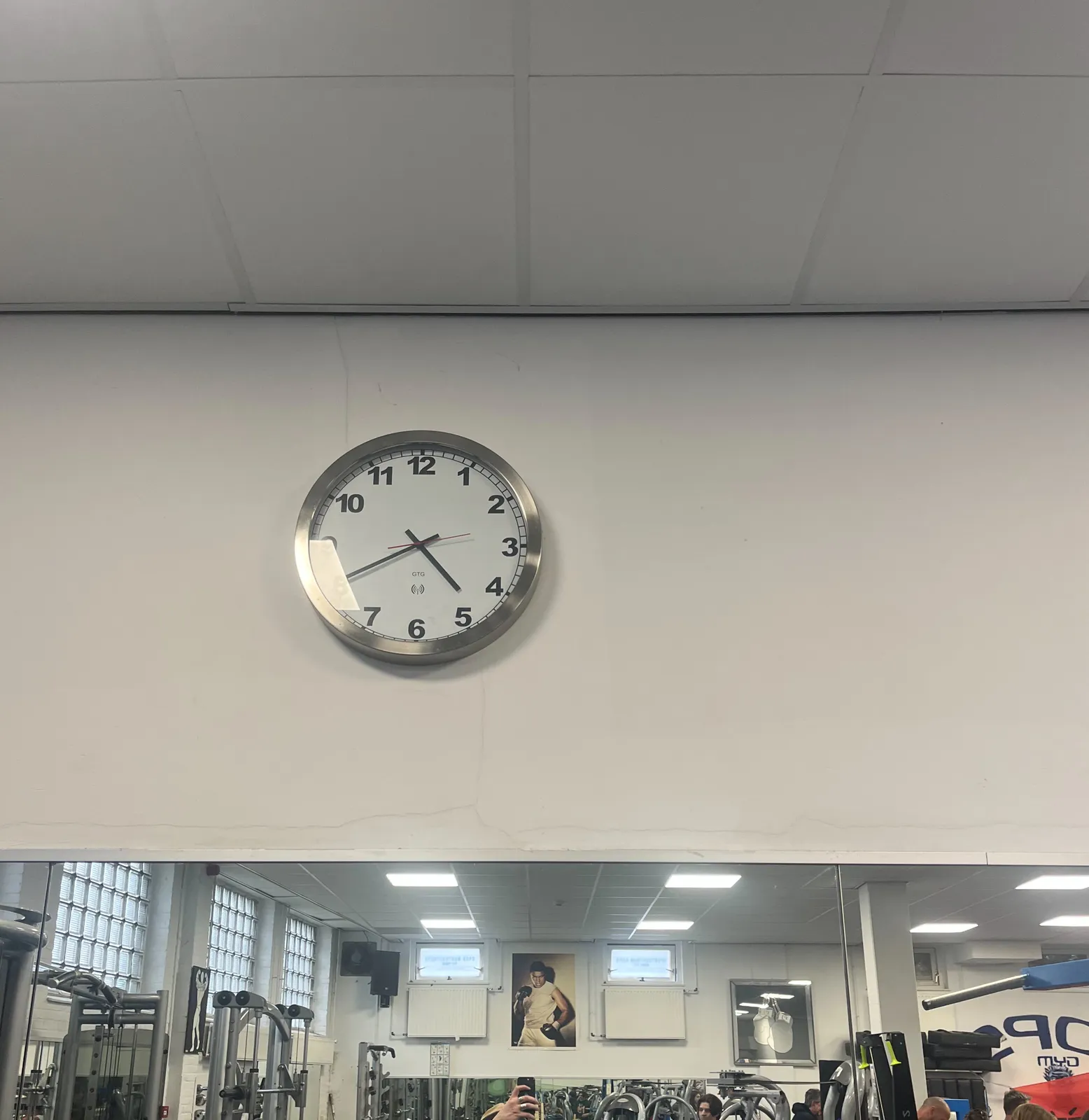 Above a mirror in a gym, there’s wall clock which points at 20 minutes to 5.