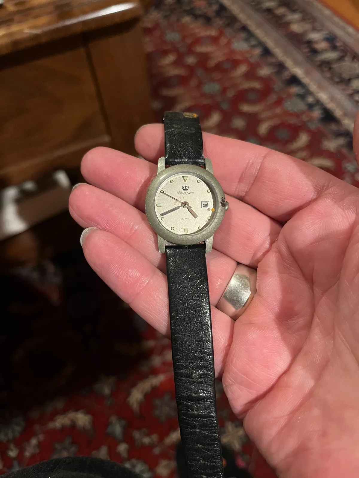 Someone is holding an old watch in their hand. In the background, blurry, an old Persian rug. The watch points at 19 minutes to five.