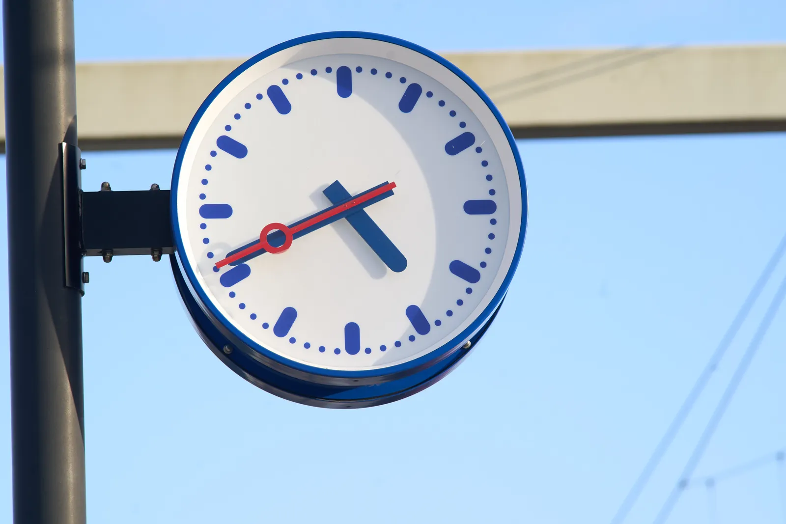 A clear blue sky behind a station clock. It points at 19 minutes to 5.