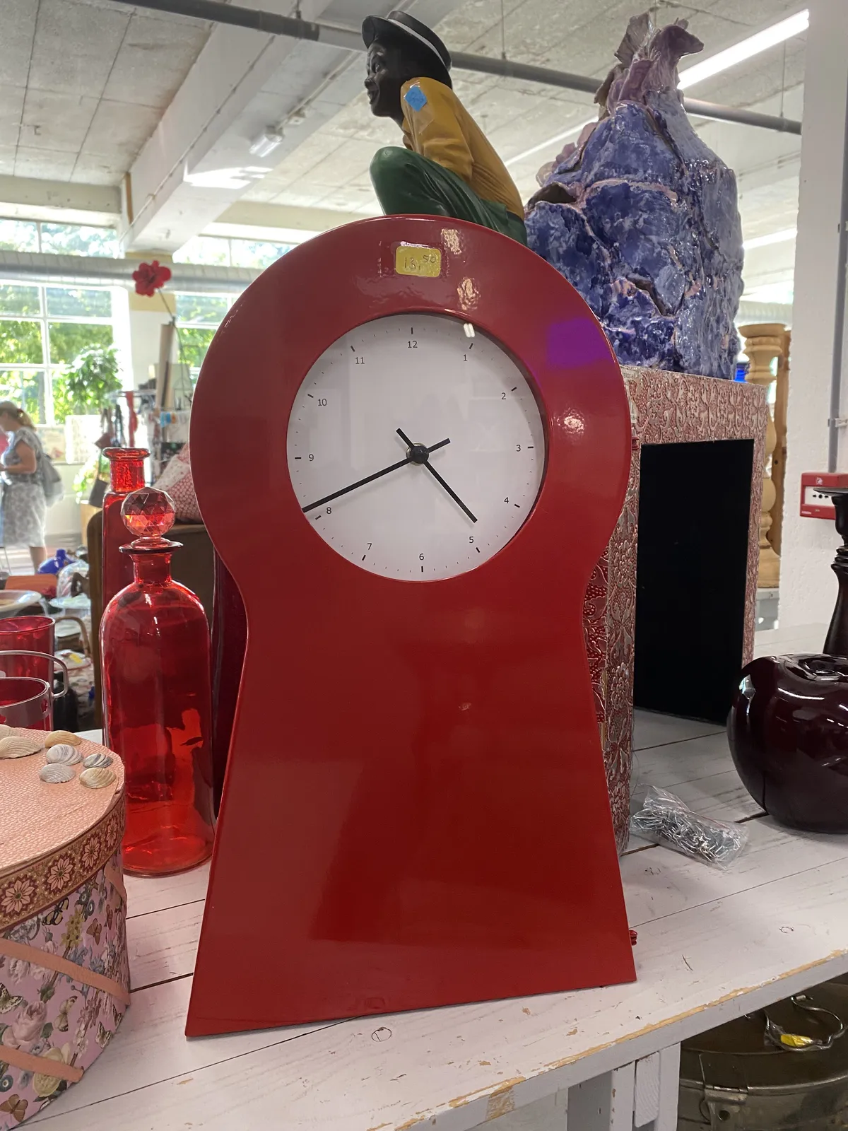A red clock in a thrift shop. It points at 19 minutes to 5.