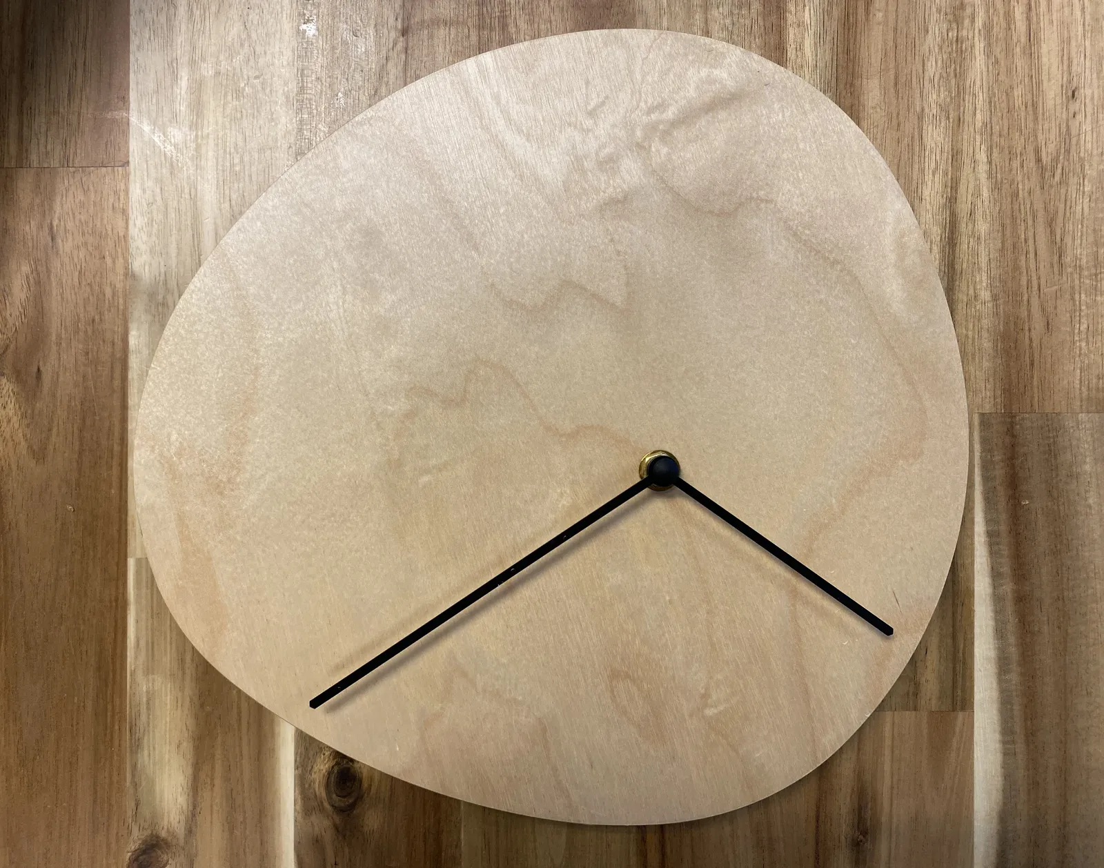 A wooden wall with a clock on it made from a wooden blob shape. The hands are not placed in the center at all. It points at approximately 18 minutes to 5.