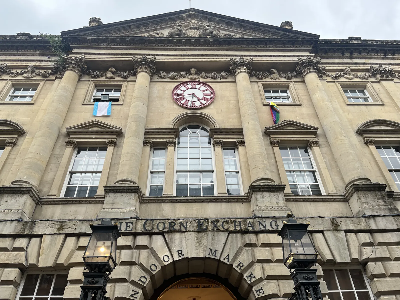 The large facade of an old, large building called the Corn Exchange. There’s a clock on this building which points at 17 minutes to five. 