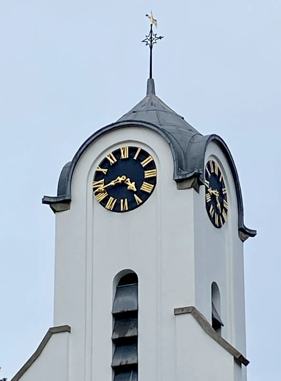 The top of a white church tower, with a clock on it that points at 17 minutes to 5.