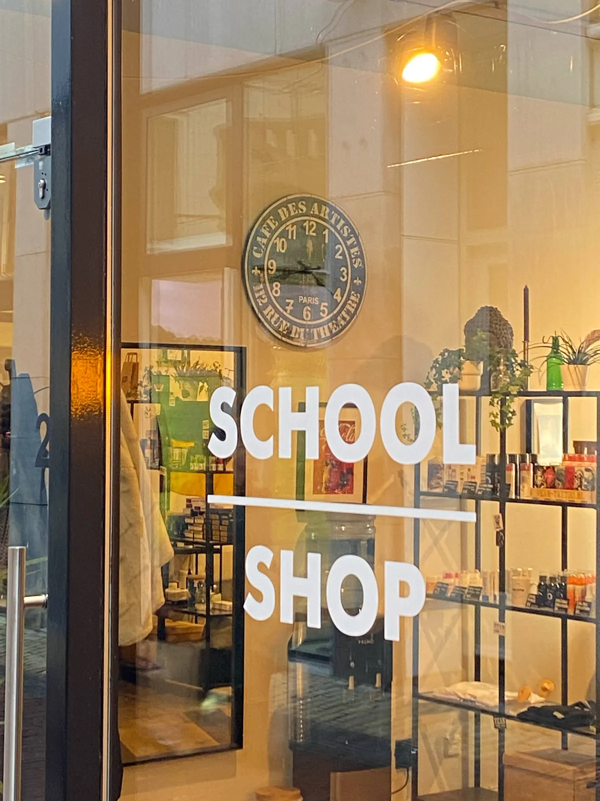 Looking through a shop window. The letters on the window say School Shop. In this shop there’s a clock on the wall which points at 17 minutes to 5.