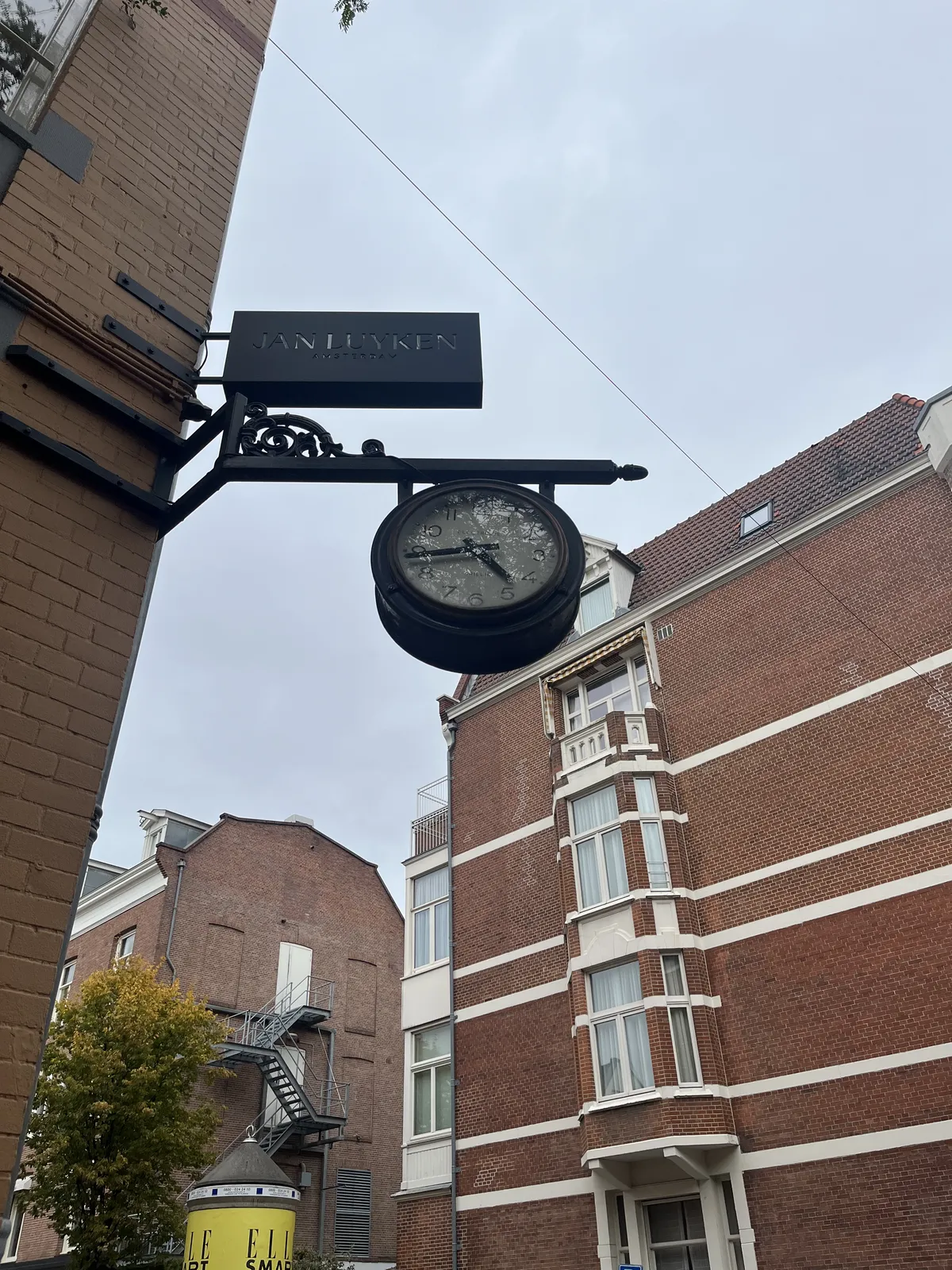 A clock hanging from a construction on the corner of a brick building. The clock points at 16 minutes to five.