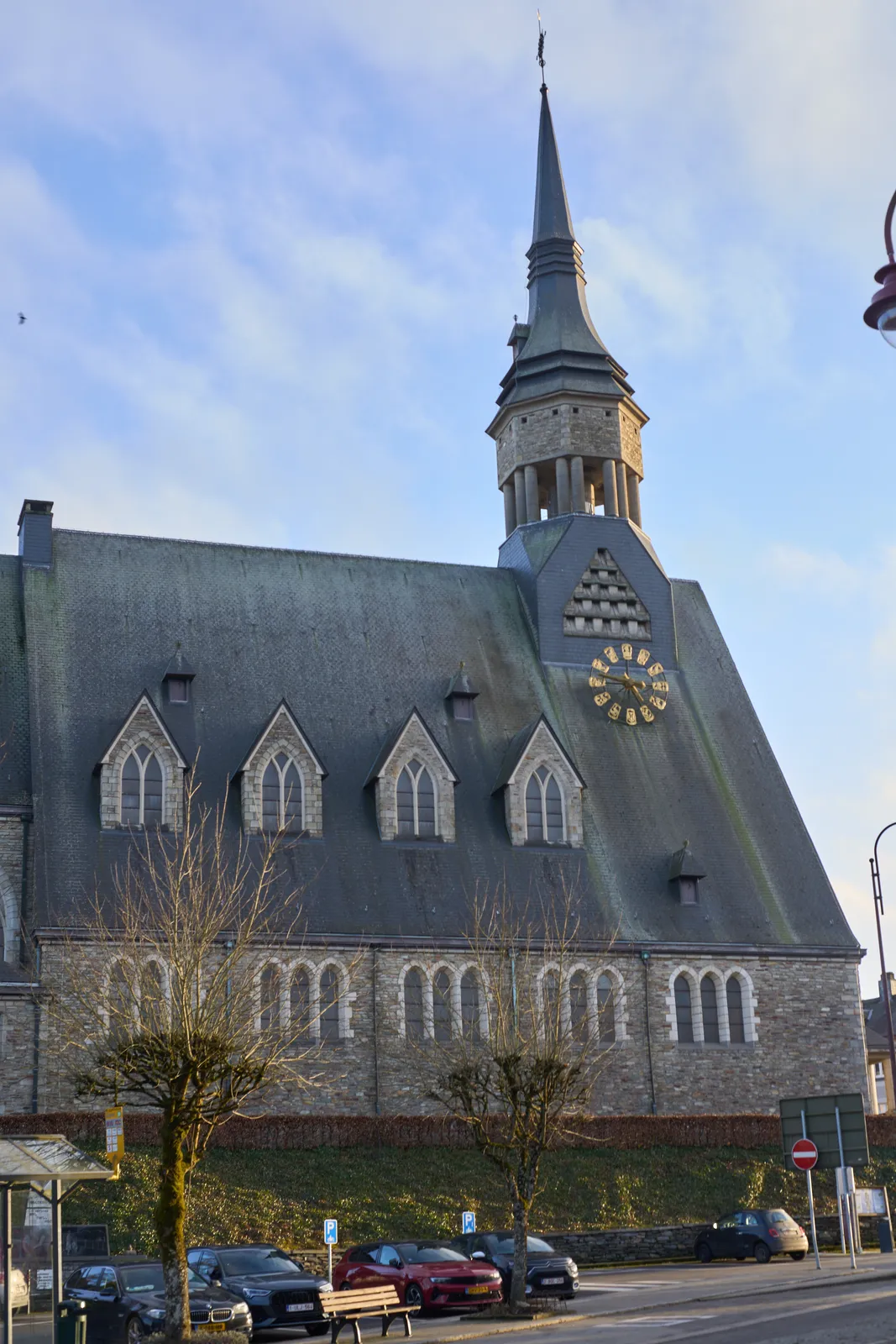 A rather large, gray church with a pointy tower and a very high roof. On the roof, not on the tower, there’s a large golden clock that points at 13 minutes to five.