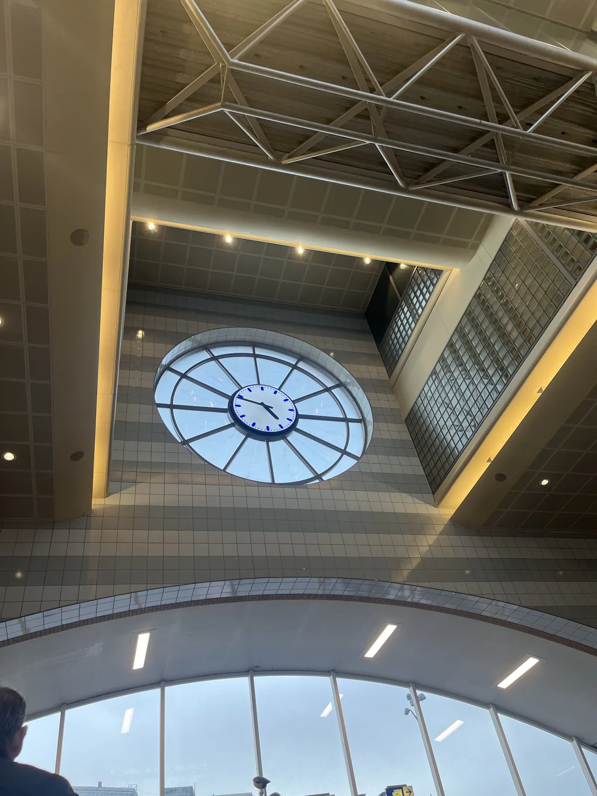 A clock built into the facade of a rather high, postmodern building. The clock points at 11 minutes to five.