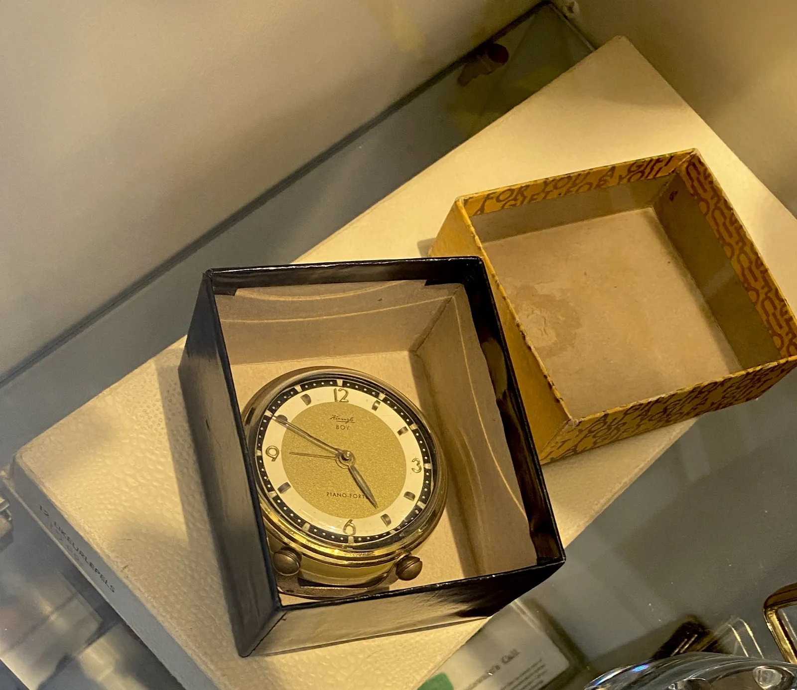 An old elegant clock in a box. On its face it says Piano Fort, and Boy with something scribbled above it. It points at 10 to five.