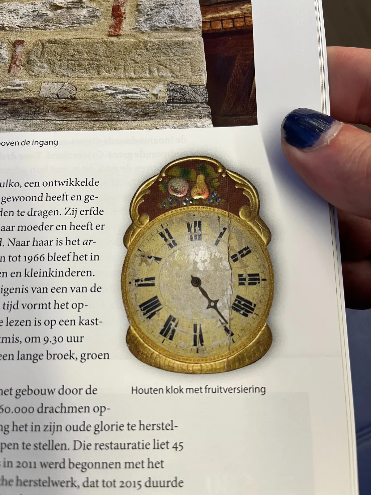 The thumb of the person who is reading this magazine is visible. In this magazine a very old clock is printed. It has just one single hand. It points at approximately 10 to 5.