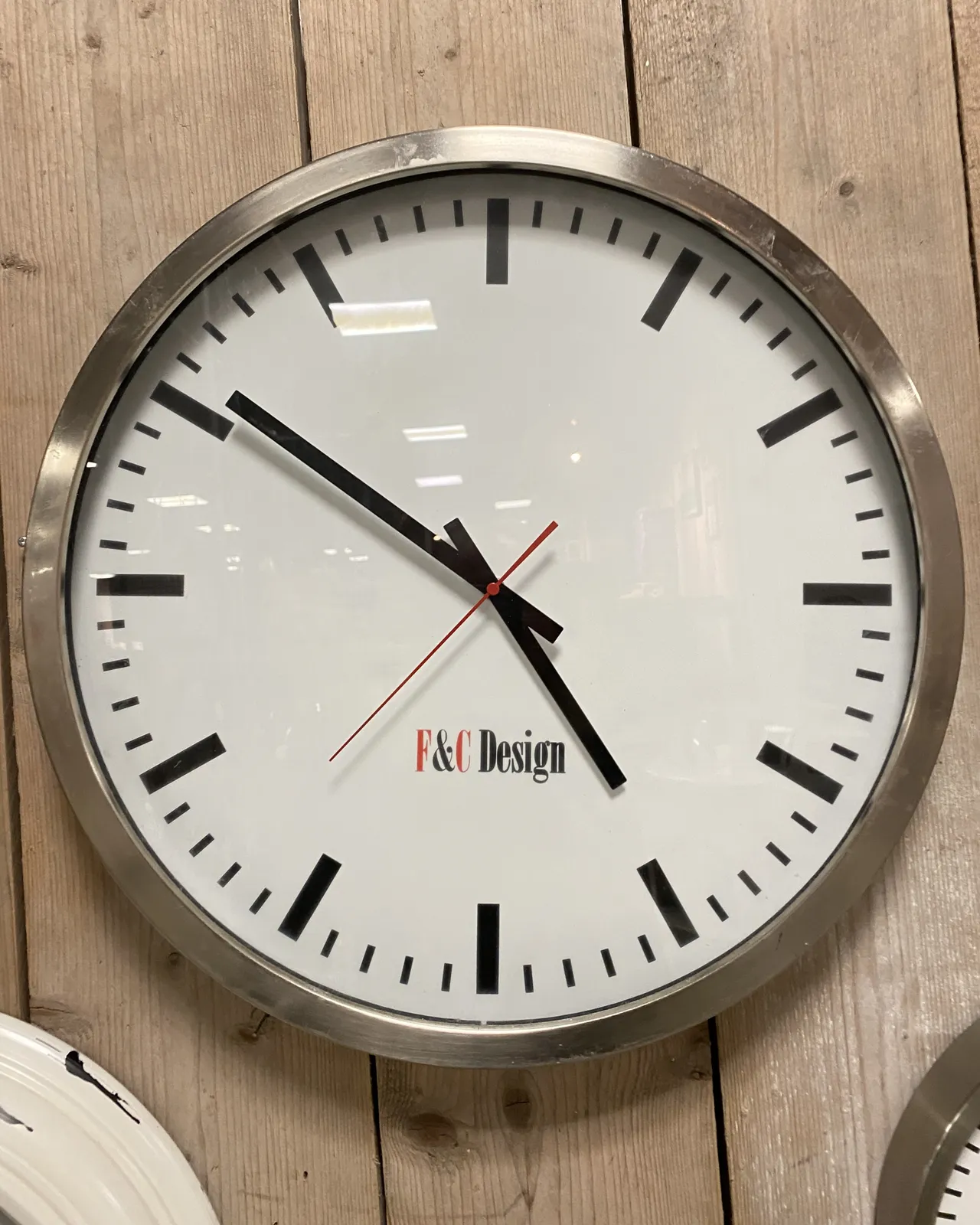 A straight forward minimalist clock, the words F&C Design are printed on its face, points at 9 minutes to 5.