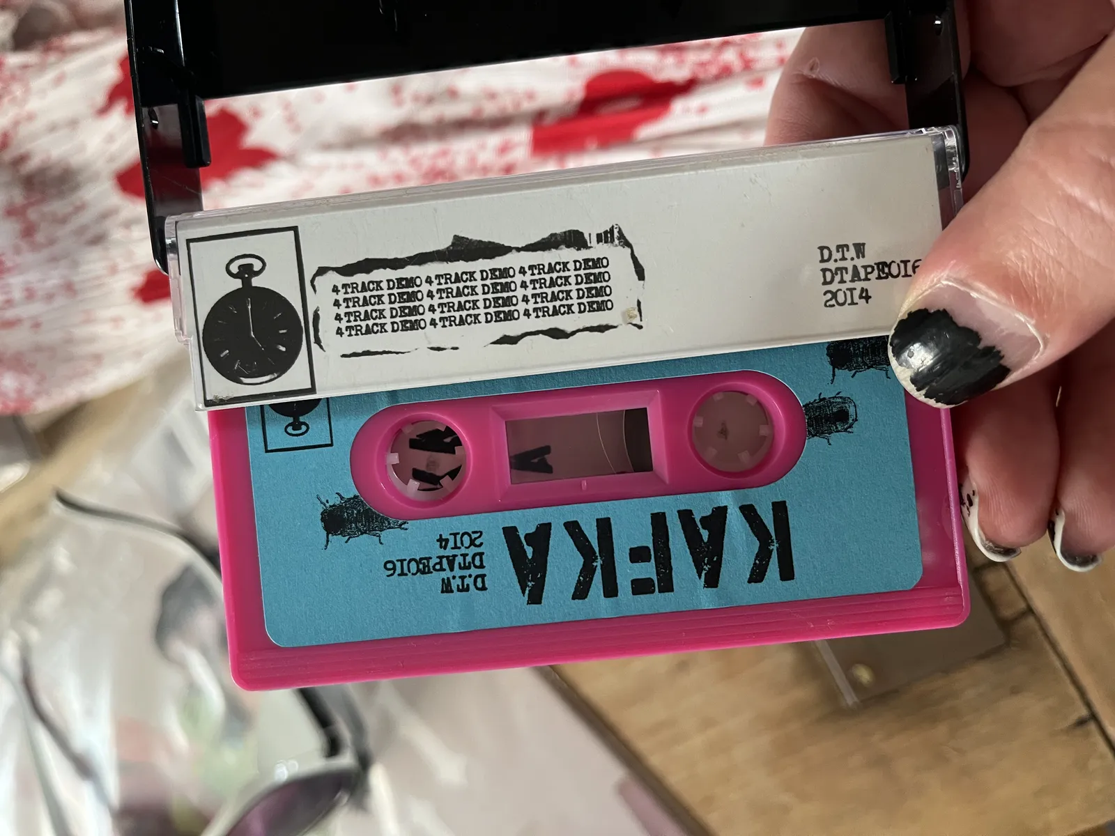 A pink and blue cassette tape in its open box. It says Kafka on the tape. There’s a clock printed on the sleeve, which points at five o’clock.