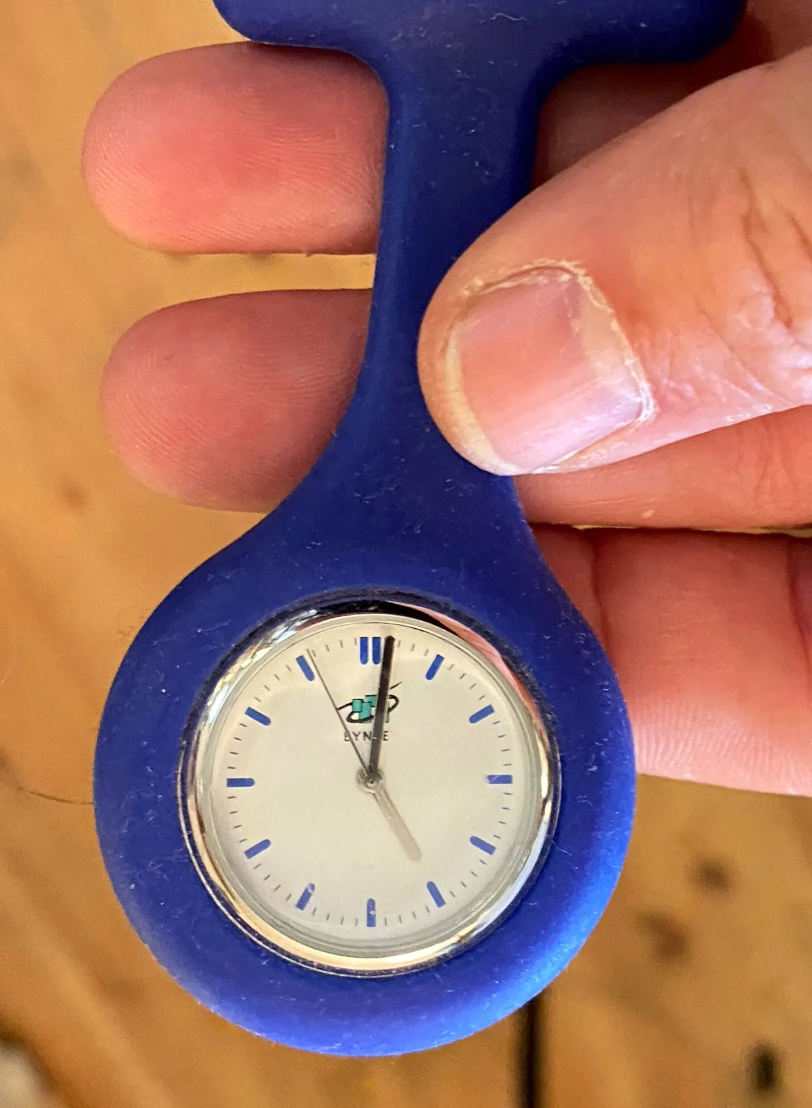 Someone is holding a small, blue, plastic clock which points at one minute past 5.