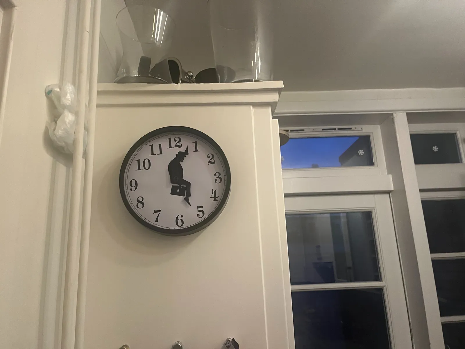 A clock in a kitchen. Its hands are made from feet, which makes it look like a character from the Ministry of Silly Walks, a classic Monthy Python sketch. The feet point at 3 minutes past 5.