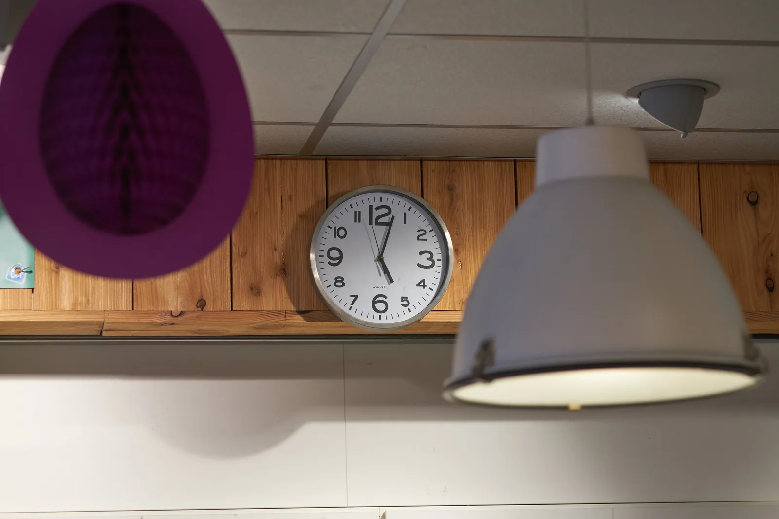 Between an industrial lamp and a piece of purple decoration there’s a clock that points at three minutes past five.