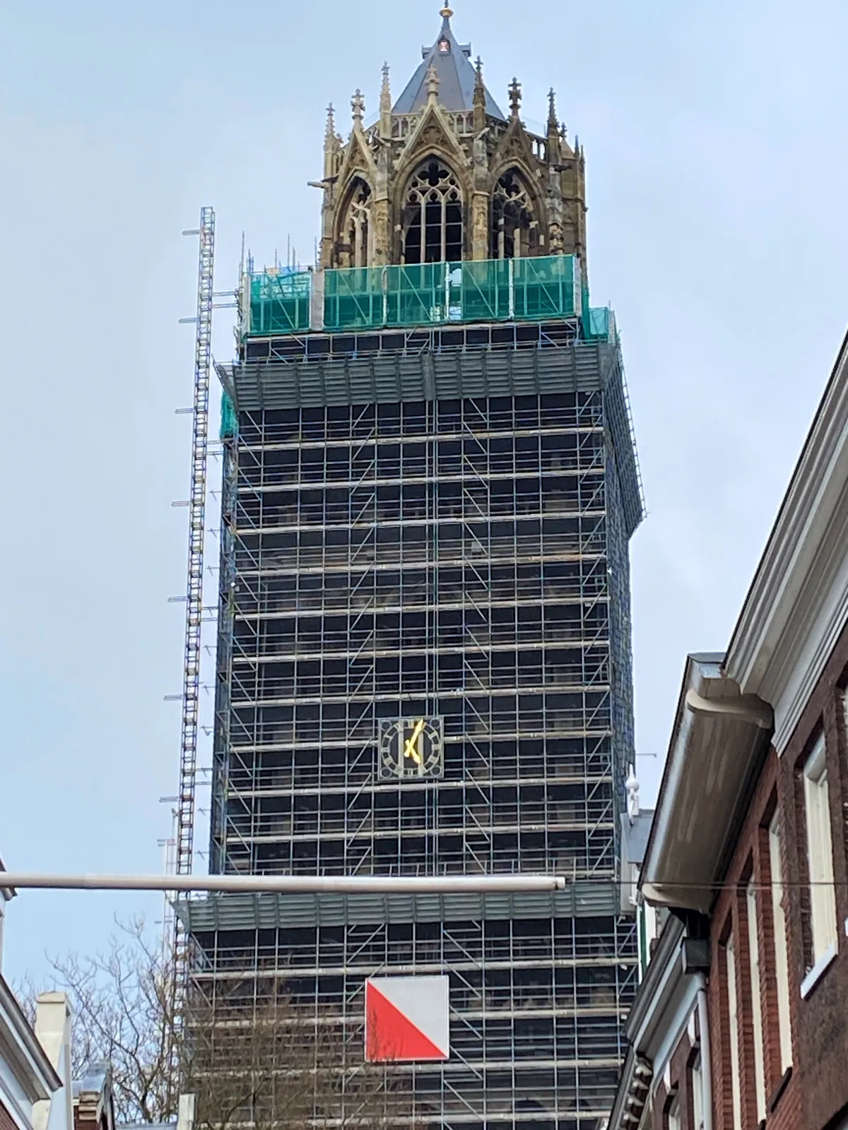 A large church tower, wrapped in scaffolding. There’s a clock attached to the scaffolding, to replace the one that’s hidden. This clock points at 4 minutes past 5. 