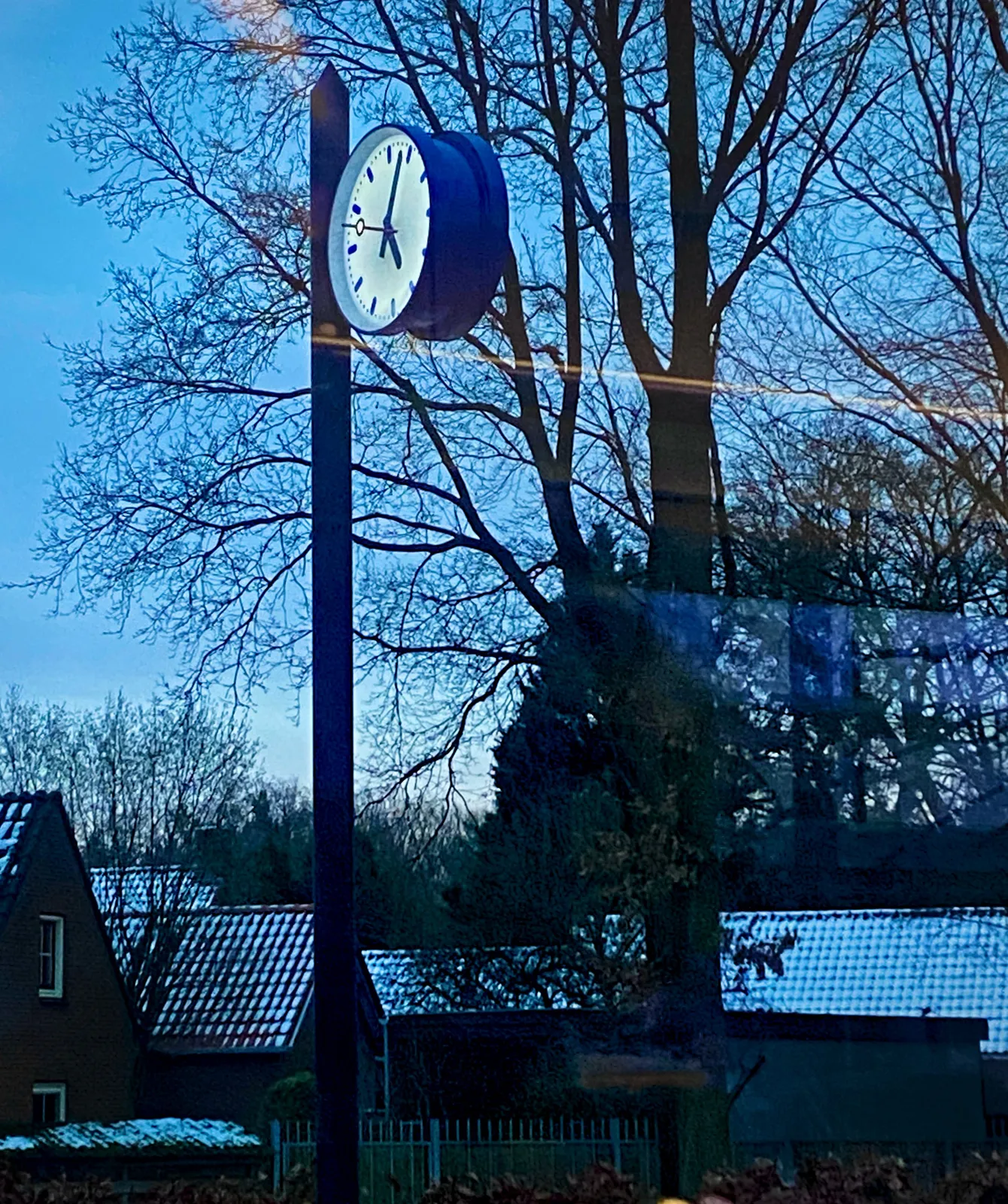 Some snow on the roofs of the houses in the distance. Closer by is a common Dutch station clock as we see them in the 2020’s. It points at 4 minutes past 5, if we correct a bit for perspective.