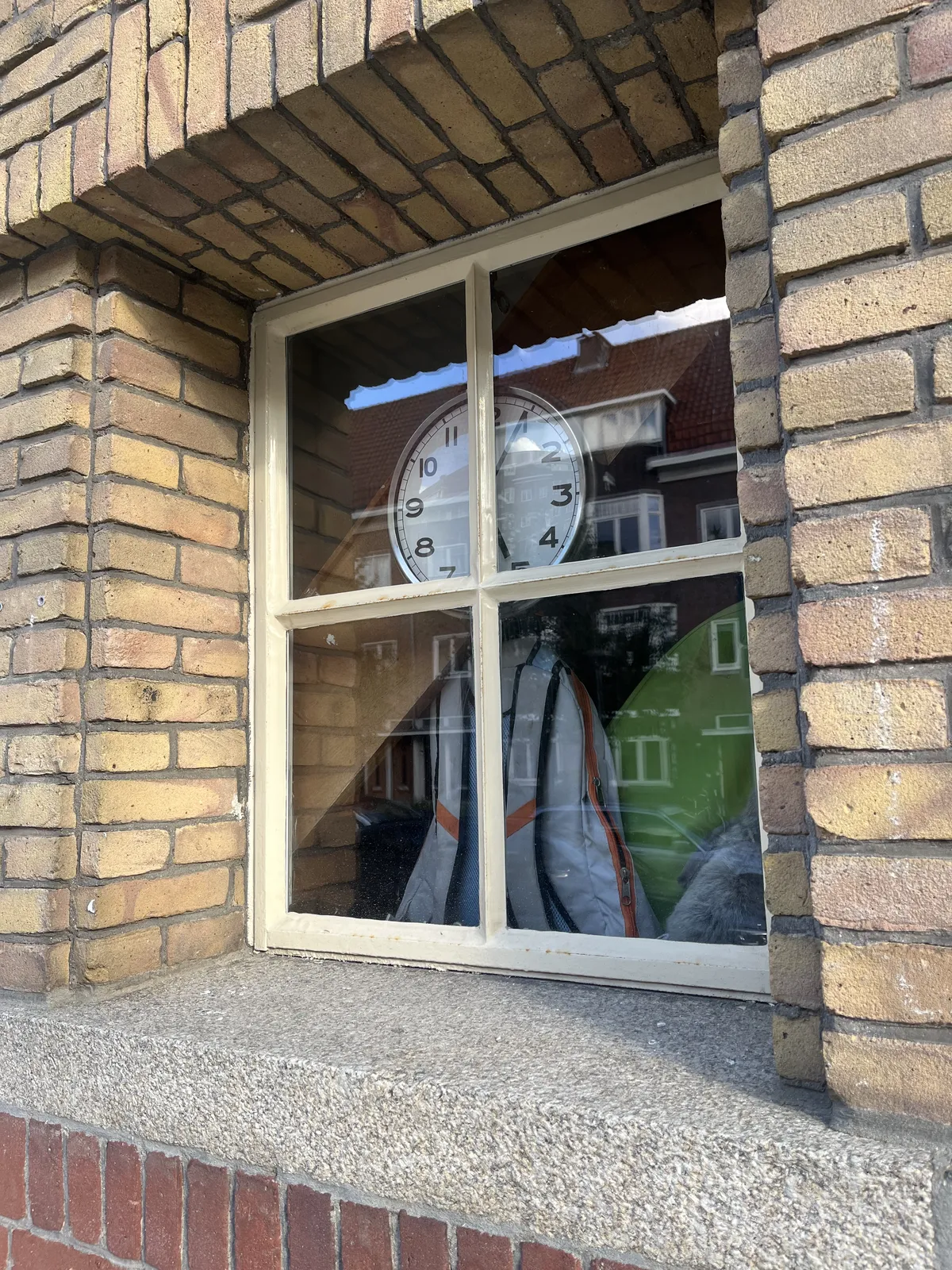 Right behind the window in a thick, brich wall there’s a clock. This clock is partly hidden behind the crossed frame of the window. But the hands are visible, and they point at 4 minutes past five.