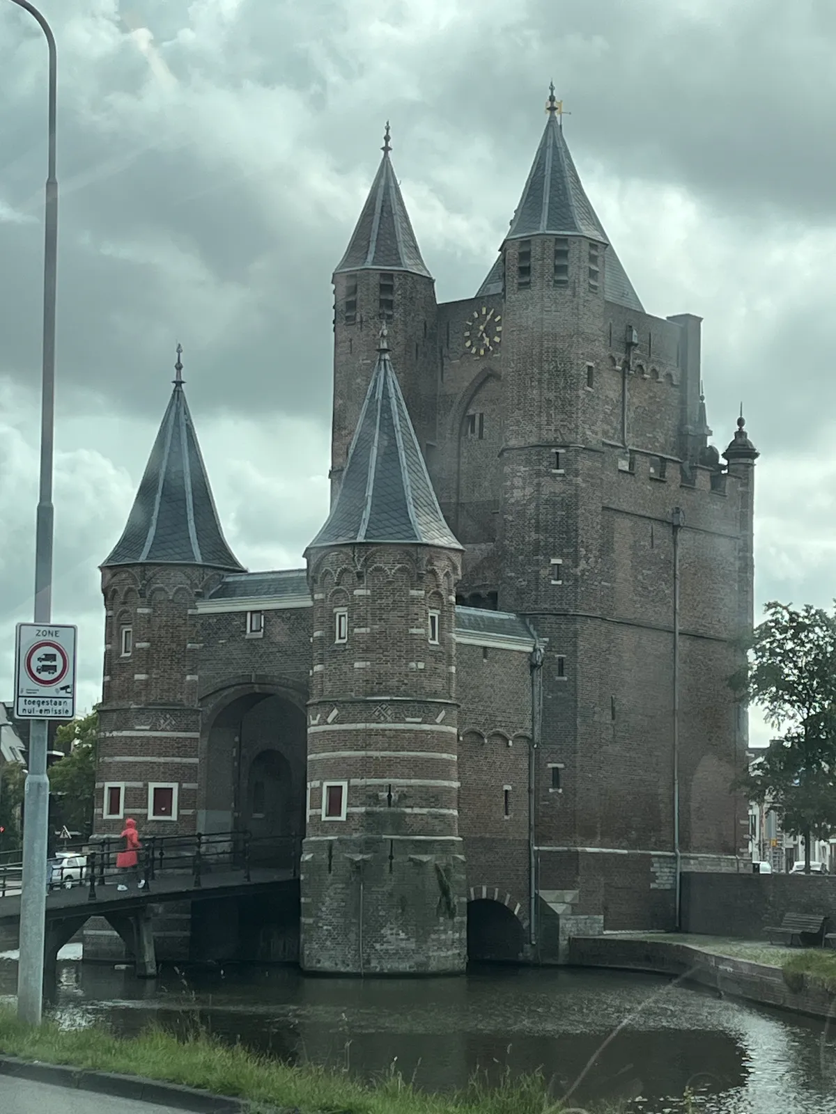 The modern lamp post, and the person in a bright red rain coat that wals on the bridge indicate that this picture is not taken in the middle ages. Otherwise this castle, or city gate, would give you this imperession. There’s a clock on top of the castle. It points at 5 past five.