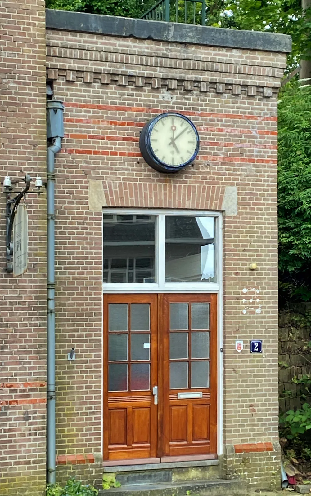 An old station clock on a small brick building. It points at 8 minutes past 5.