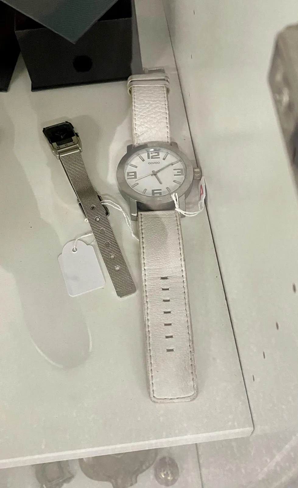 A white watch, laid down on a white cloth. It points at 9 minutes past 5.