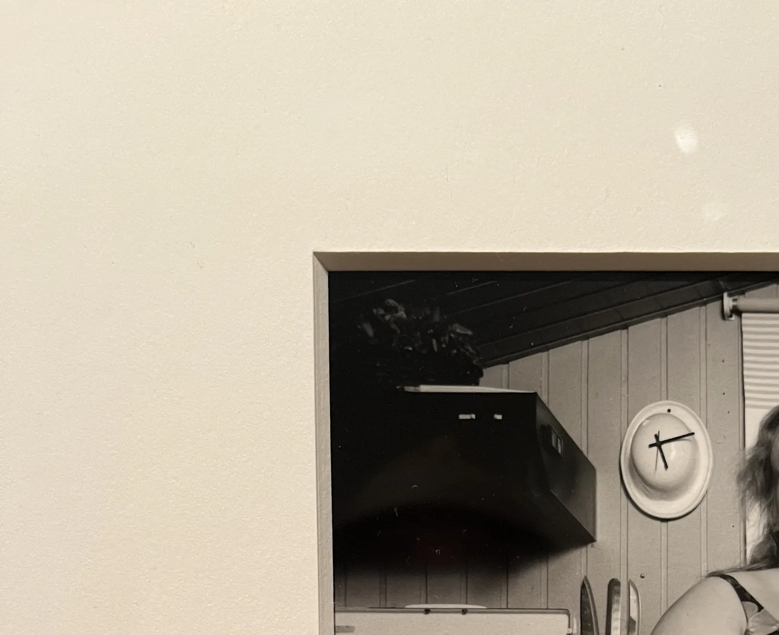 A pucture taken from the top left corner of a framed black and white picture. There’s a wall clock made from a helmet in this picture. It points at 11 minutes past five.