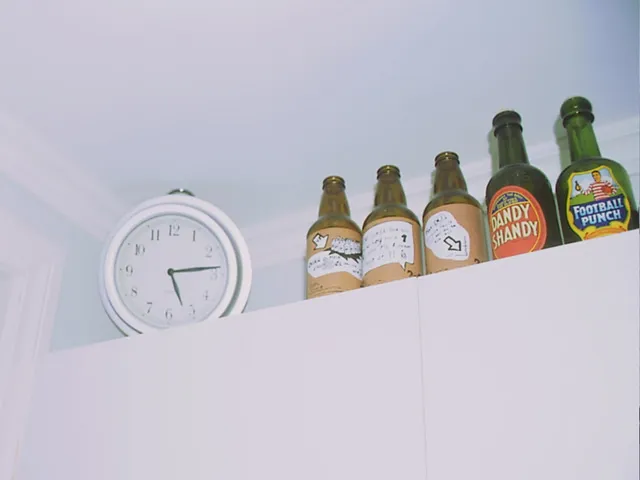 There are five bottles standing next to this clock. The clock points at 13 past five.