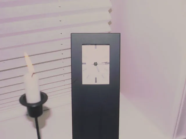 A candle burns, and the clock next to it points at fourteen minutes past five.