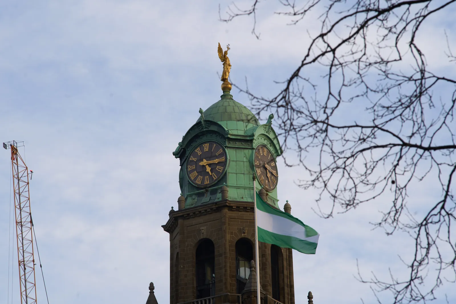 A wintery tree, a crane and a church tower with a clock that points at a quarter past 5.