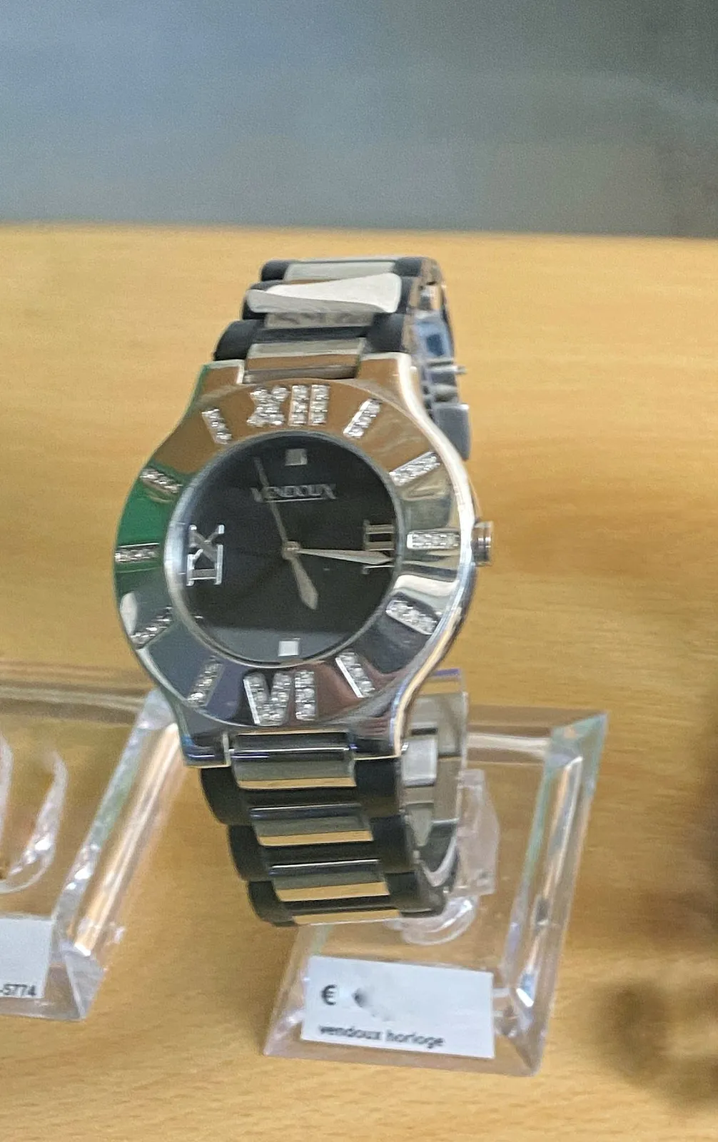 A silver coloured watch with quite a few diamonds. It points at 16 past 5.